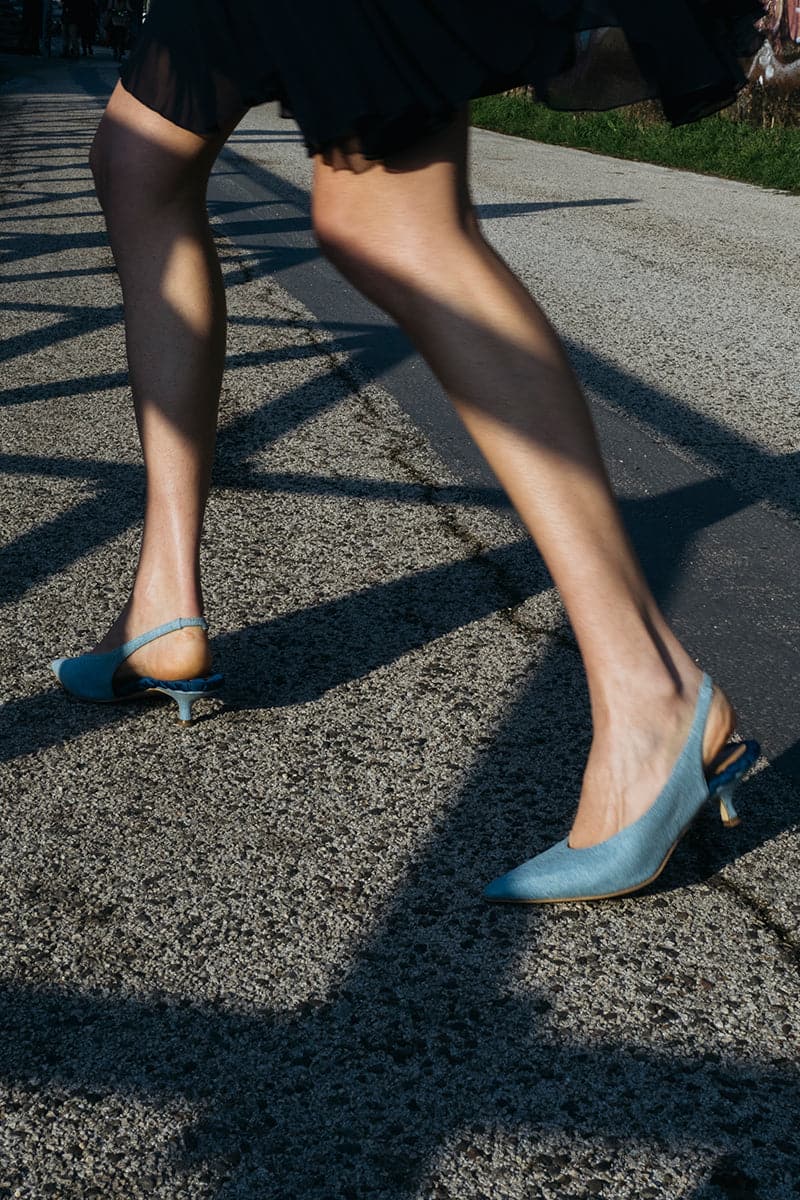 A pair of AERA Silvana blue denim slingback pumps with pointed heels and open toe design on a white background.
