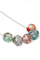 Multicolor SOPLO necklace by SALVÁREA featuring layered, vibrant pendant necklaces on a neutral background.