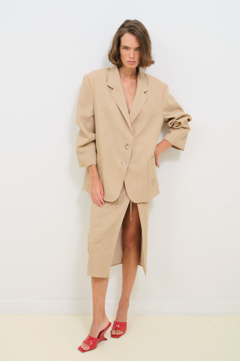 Light beige linen pencil skirt with intricate embroidery, midi length, by TAGG, shown on a model.