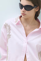 Pink embroidered oversized shirt by TAGG with detailed stitching, relaxed fit, and casual style, displayed on a hanger.