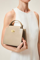 TUSTING Clara taupe top handle bag with sleek design and structured shape, featuring a top handle and elegant finish.