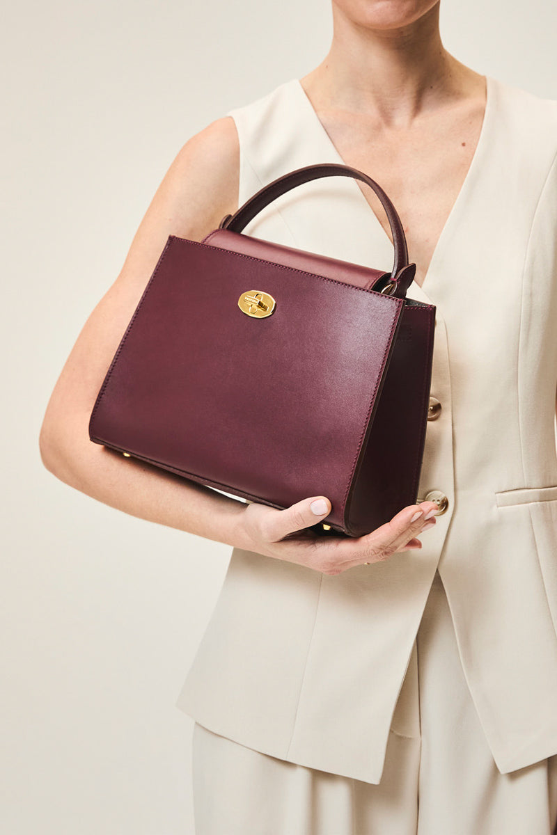 TUSTING Clara Grande oxblood top handle bag with sleek design and sturdy handles, showing the elegant leather finish.