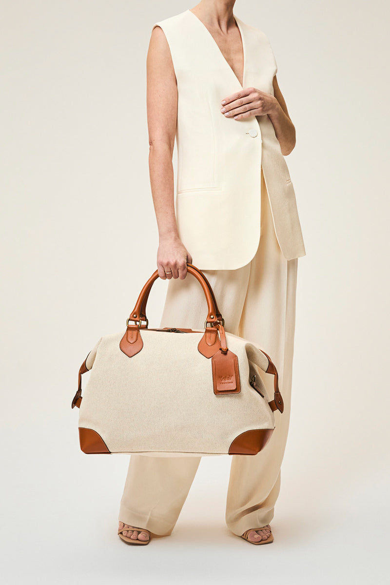 TUSTING COMO EXPLORER medium top handle bag in black leather with gold hardware and adjustable strap.