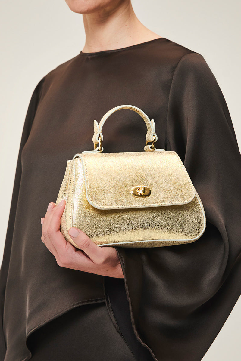 Mini Holly in gold suede, TUSTING top handle bag with elegant design and gold-tone accents, shown in a close-up image.