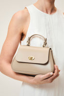 Mini Holly taupe top handle bag by TUSTING, featuring a compact design with a sleek, structured silhouette and top handle.