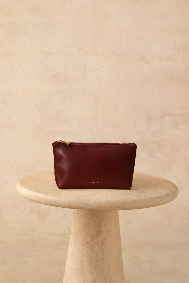 TUSTING leather top handle pouch in oxblood color, featuring a sleek design and compact size for stylish everyday use.