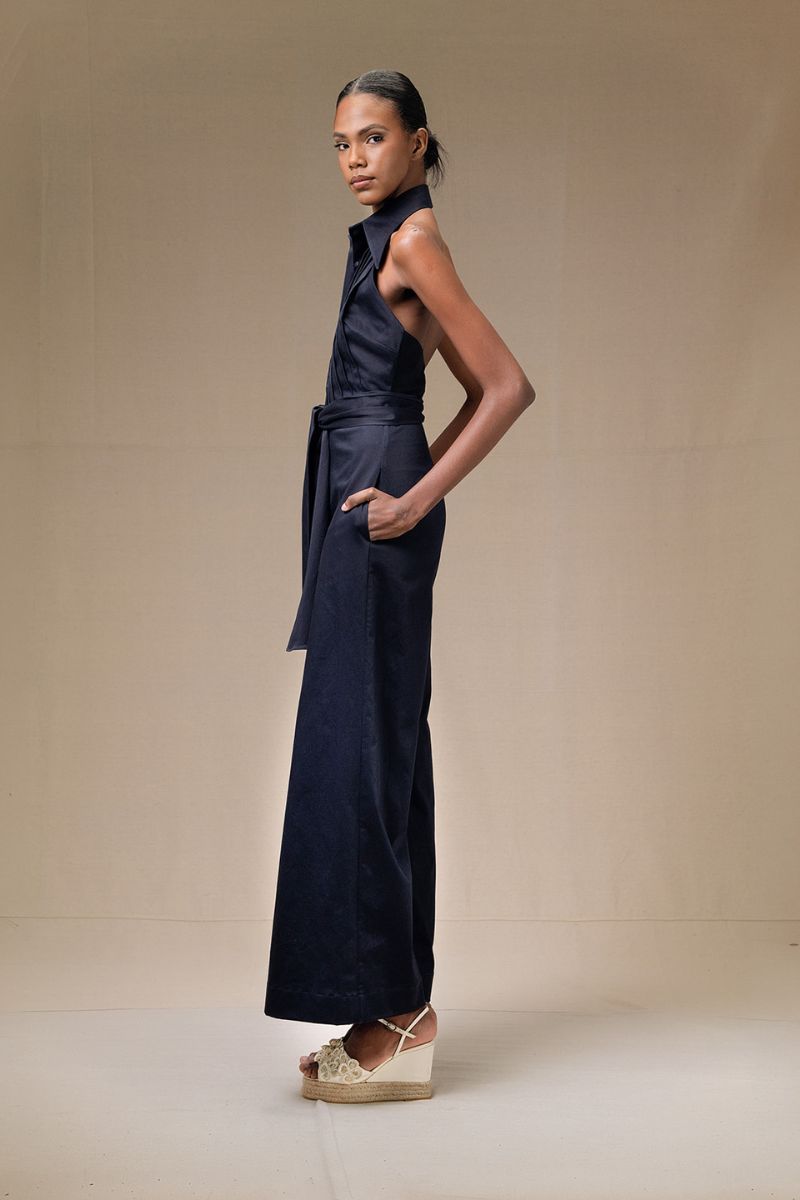 Navy blue wrapped jumpsuit by ANA + MARIA featuring a fitted waist and long sleeves, displayed on a neutral background.