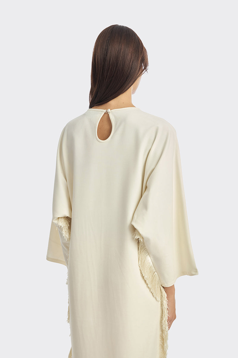 Ivory white maxi dress with long sleeves and fringe detail by Stolen Stores, styled with a relaxed, elegant fit.