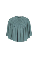 Hand-smocked TIYA cape in Saxon color by MASTANI, featuring intricate detailing and a stylish top design.