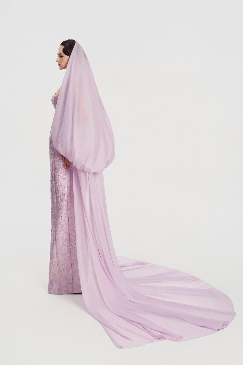 Elegant jacquard gown with a hooded veil cape by Tracy Studio, featuring intricate fabric patterns and flowing maxi dress design.
