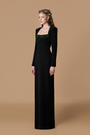 Black crepe de chine silk-lined gown with a trapeze neckline and long sleeves, featuring elegant green crystal embellishments.