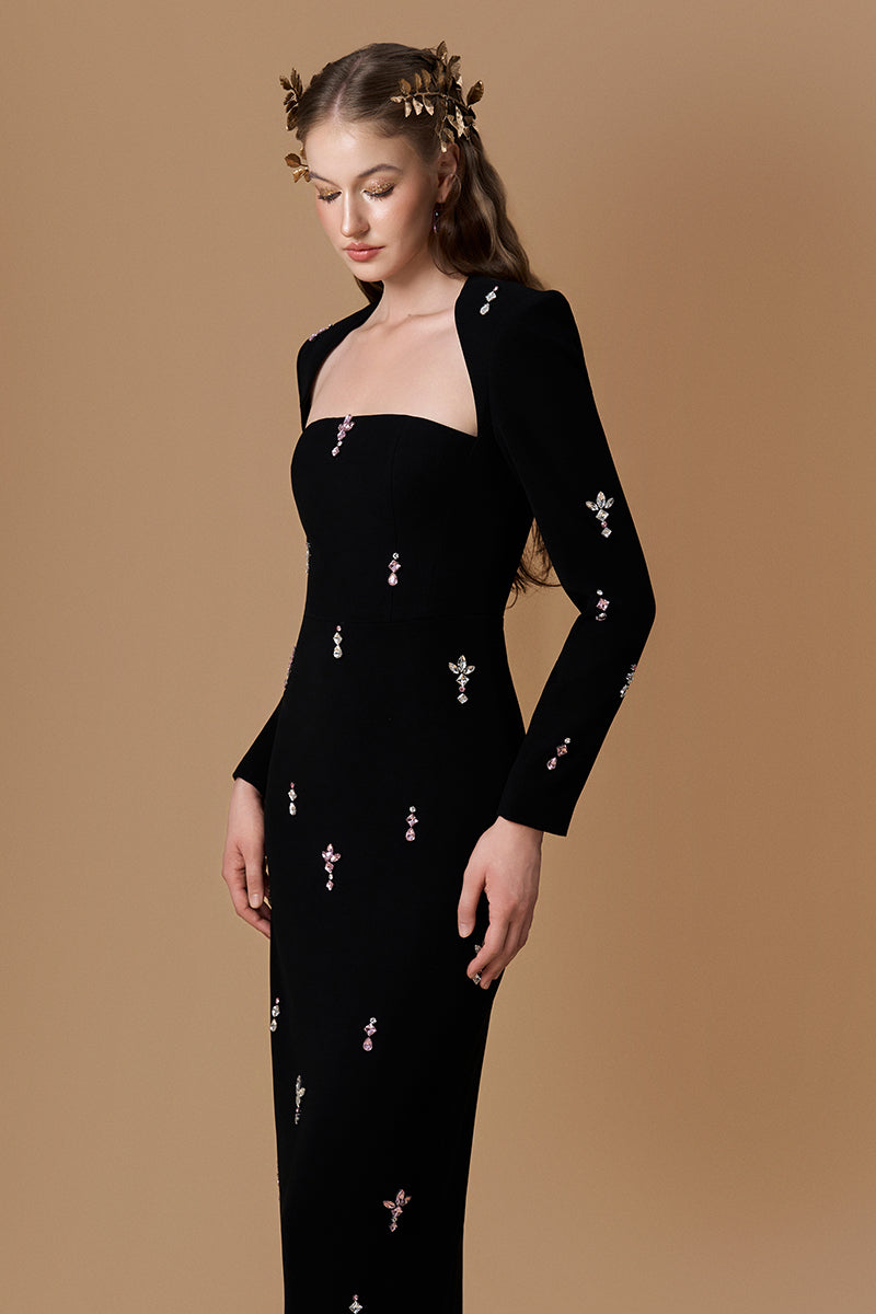 Black crepe maxi dress by I.H.F with a trapeze neckline, long sleeves, and pink stones detail on the elegant column gown.