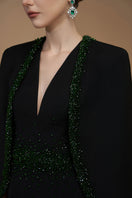 Black emerald gown by I.H.F featuring a V-neck, column silhouette, crepe and silk lining, with elegant cape sleeves.