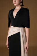 Black and ivory crepe silk lined gown by I.H.F featuring a V-neck, asymmetric draped detail, and mini cape.