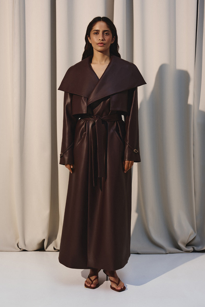 Dark brown vegan leather trench coat by Kris Marán, displayed hanging with a classic collar and long sleeves.