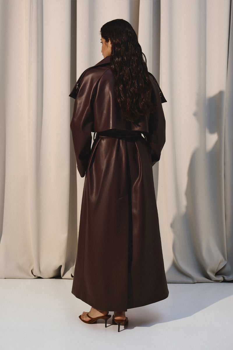 Dark brown vegan leather trench coat by Kris Marán, stylish and sleek, shown hanging on a minimalist clothing rack.
