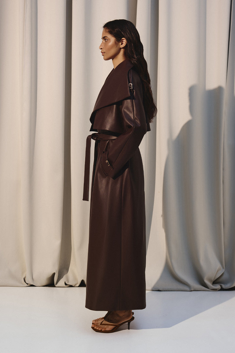Dark brown vegan leather trench coat by Kris Marán, shown on a model, featuring classic design and sleek silhouette.