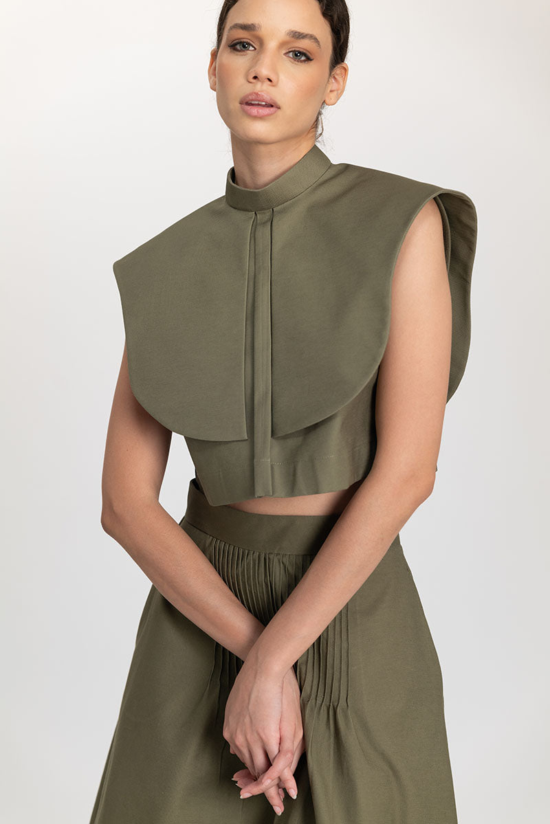 Olive drab cropped top by ANA + MARIA with a fitted silhouette and short sleeves, styled casually on a model.
