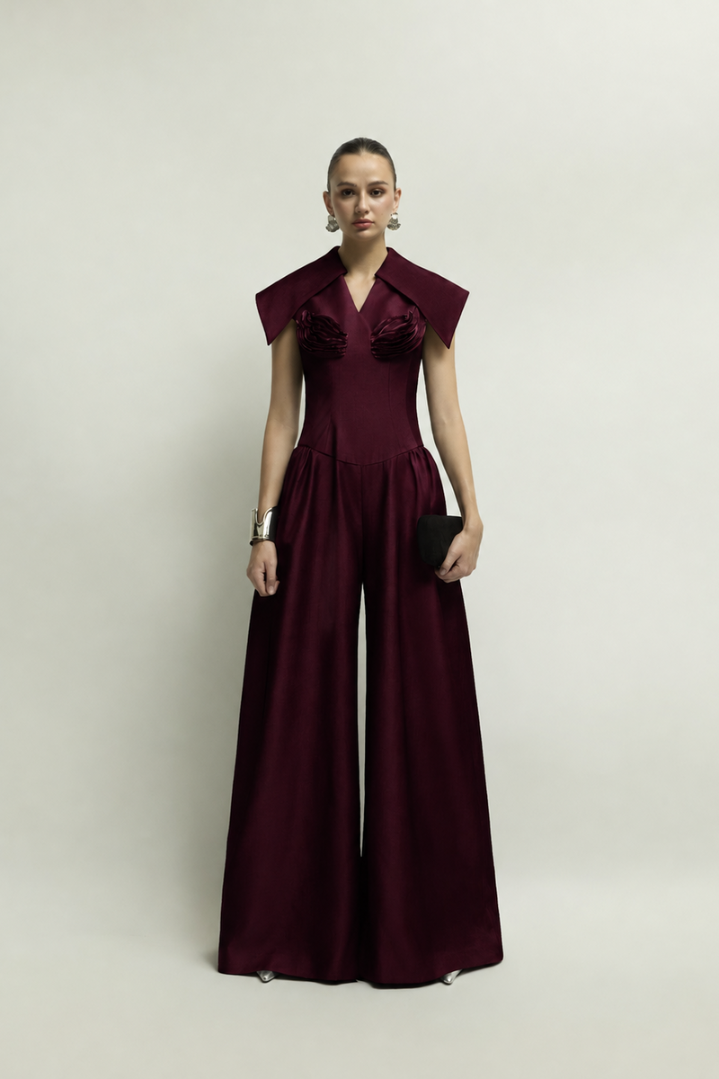 Jenny K Tran Zelie burgundy jumpsuit shown on a hanger with a fitted waist and wide-leg trousers.