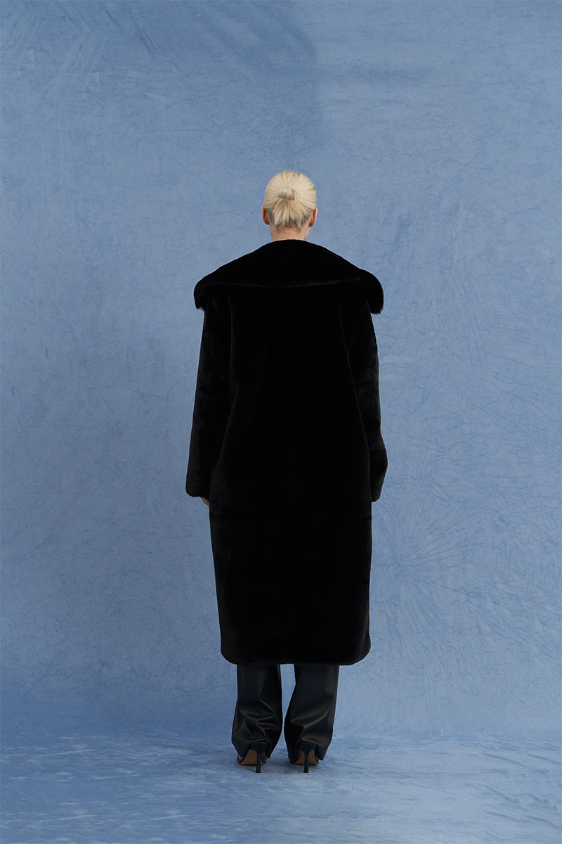 Black oversized shearling coat by JINSUN, shown from the back with plush shearling lining and wide collar detail.