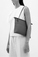 Black pebble leather FRIDA flat tote bag by behno New York shown on model, featuring shoulder straps and sleek design.
