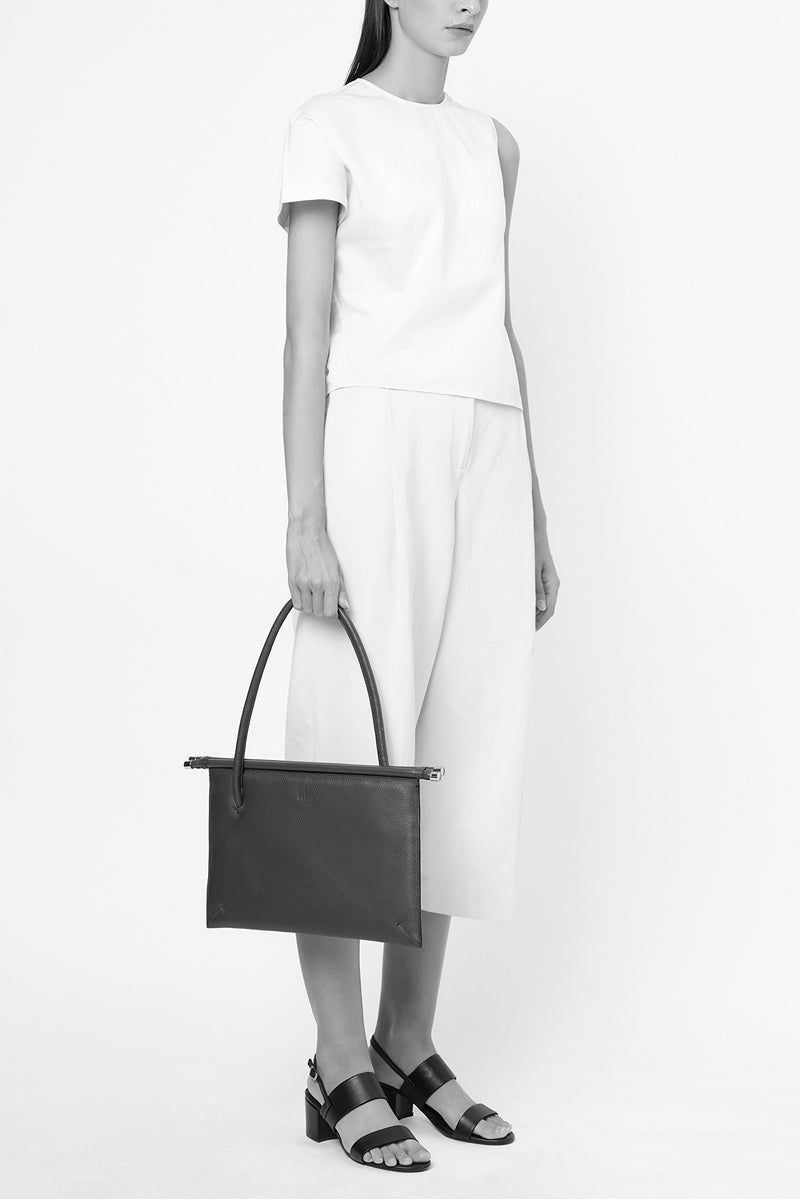 Black Pebble leather Frida Flat Tote shoulder bag by behno New York, shown on body with sleek design and minimalist style.