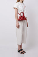 Red Behno New York Tina Baguette Mini Nappa ruched top handle bag shown on model, highlighting its compact design and elegant style.