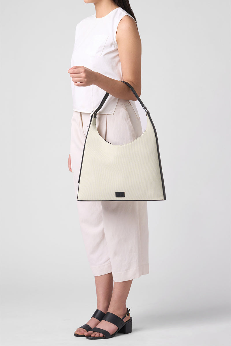 Large beige and black canvas shoulder bag by behno New York, shown on body with a sleek, modern design and spacious interior.