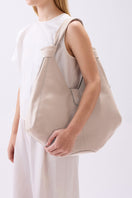 Large Nelli Hobo shoulder bag in pebble leather in bone color by behno New York, shown on body with adjustable strap.