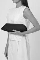 Behnò New York Elizabeth Baguette Mini Clutch in hematite with sleek, curved design and metallic finish, held on body.