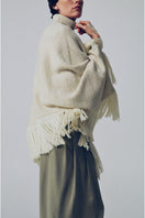 DELEGAN Milk Blush Poncho cardigan displayed on a model, showcasing soft fabric and stylish fit in a fashion campaign setting.