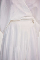 Close-up of a white maxi skirt by DELEGAN featuring hand-embroidered tie detail and flowing fabric.