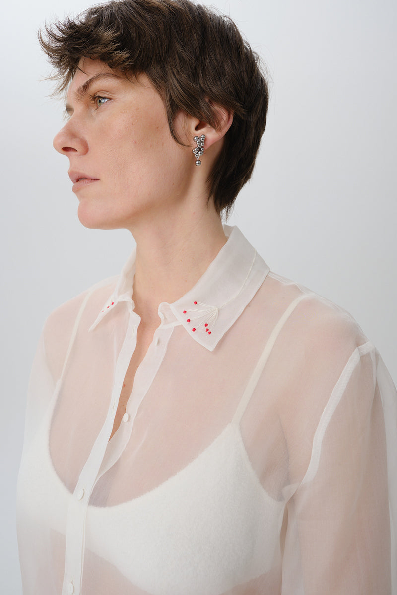 Close-up of a red silk shirt by DELEGAN, showcasing smooth fabric and detailed stitching.