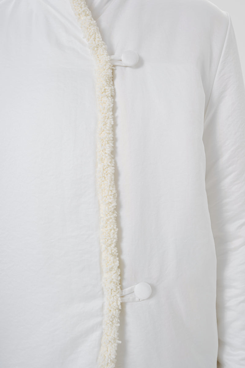 Close-up of a white DELEGAN jacket showing fabric texture and detailed stitching on the jacket's front.