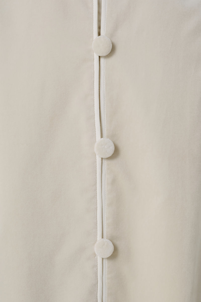 Close-up of a luxurious ivory velvet coat by DELEGAN, showcasing soft fabric and elegant stitching details.