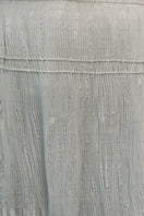 Close-up of a white maxi skirt with hand-embroidered tie detail from DELEGAN, showcasing intricate embroidery and fabric texture.