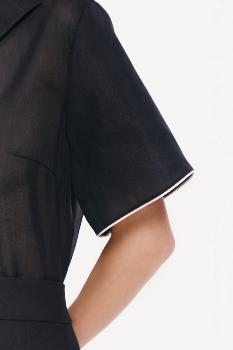 Close-up of a black DELEGAN shirt with white edging, showing detailed stitching and fabric texture.