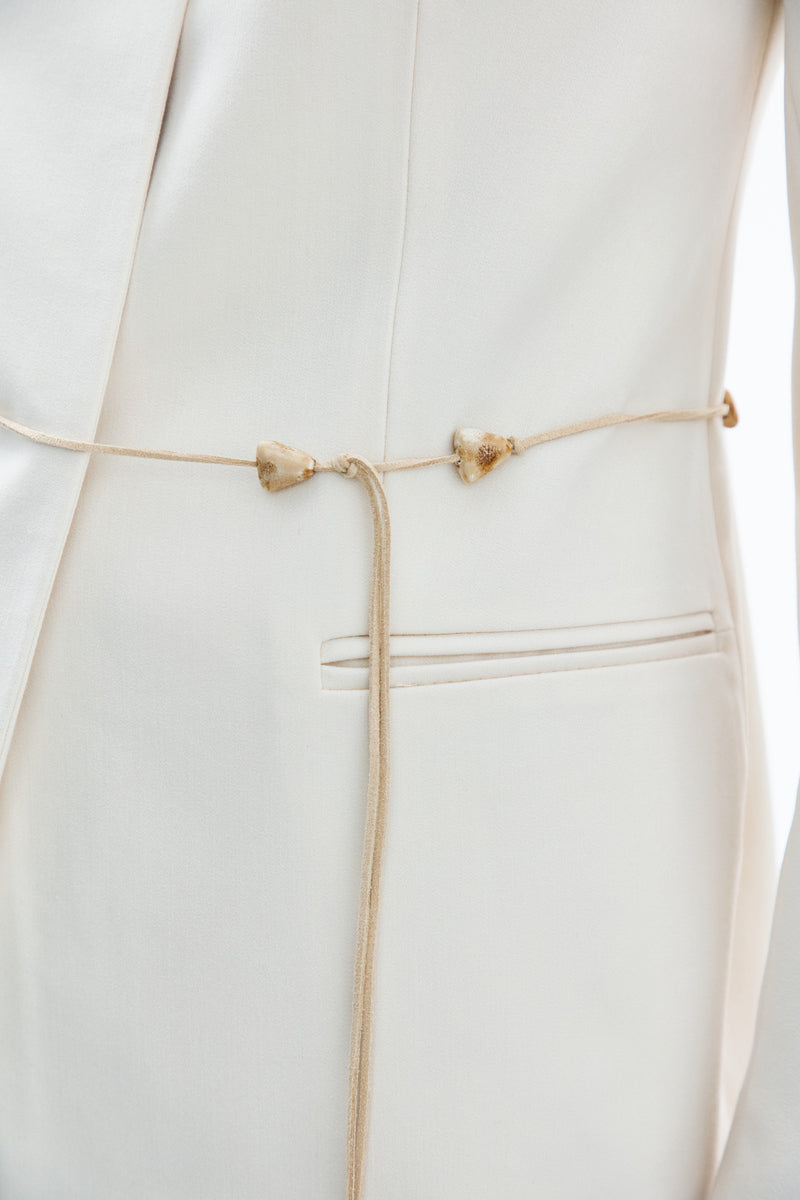 Close-up of a white and gold belted DELEGAN jacket showing fabric details and stylish belt design.