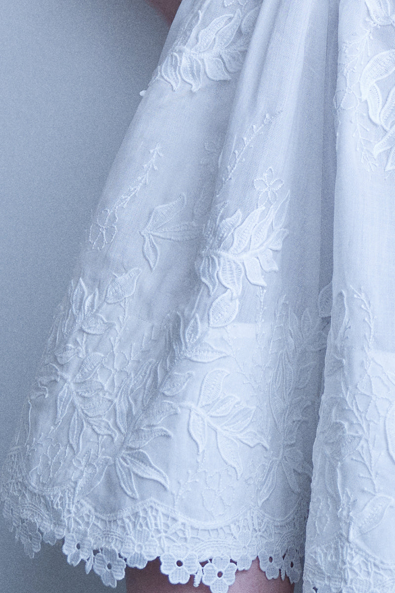 AISA Emma white mini dress displayed on a hanger, showcasing its simple yet elegant design and lightweight fabric.