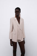 SÉLONE Helia wrap blazer in stone color, tailored blazer with a wrap design and long sleeves, shown on a model.