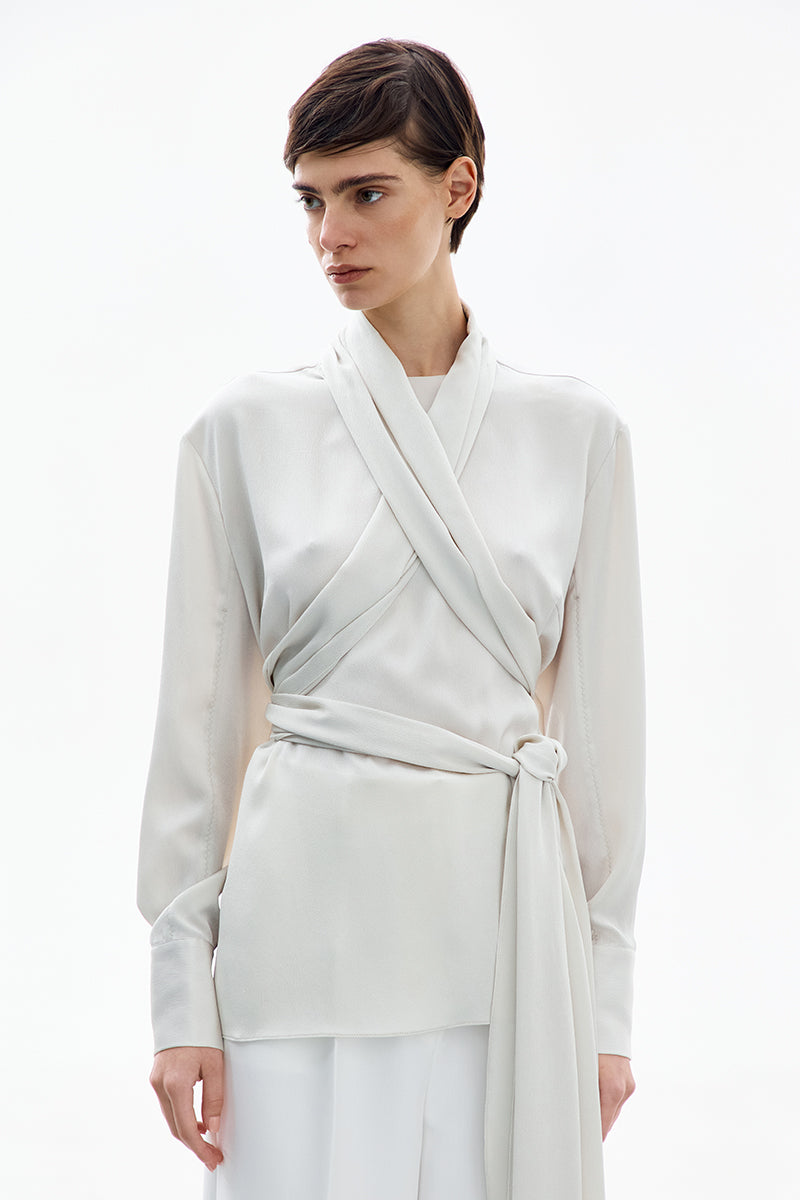 Pearl white wrapped blouse by Delegan, featuring elegant design, long sleeves, and a stylish fit, perfect for sophisticated casual wear.