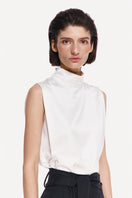 DELEGAN Pearl Silk High Neck Top, elegant cream-colored silk blouse with a high neckline and smooth texture, styled for sophisticated wear.