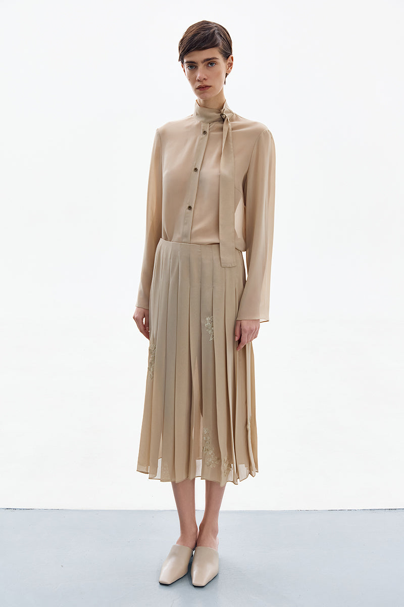 Golden nude pleated midi skirt by DELEGAN, showcasing a high-resolution image of the elegant, flowing fabric and detailed pleats.