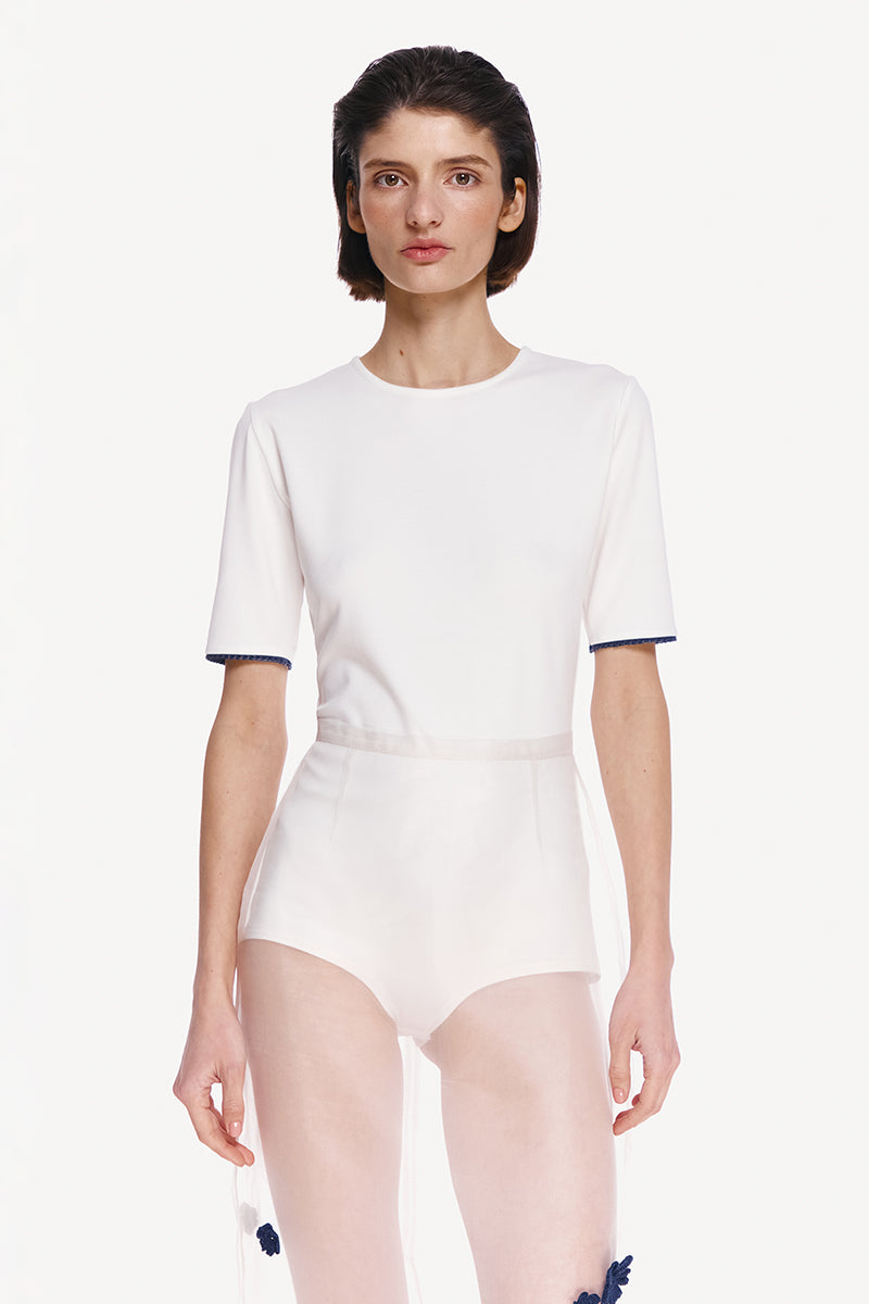 White short sleeve bodysuit by Delegan, close-up view showing fitted style and smooth fabric, ideal for casual and layered outfits.