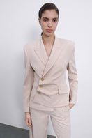 SÉLONE Oris asymmetric tailored blazer in warm beige, featuring a modern twist and structured fit, displayed on a hanger.