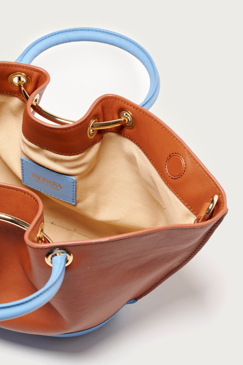 Saonara Mini Capazo top handle bag in caramel and blue sky with woven straw design and leather handles.
