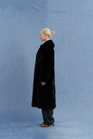 Black oversized shearling coat by JINSUN shown from the side, featuring a plush shearling collar and relaxed fit.