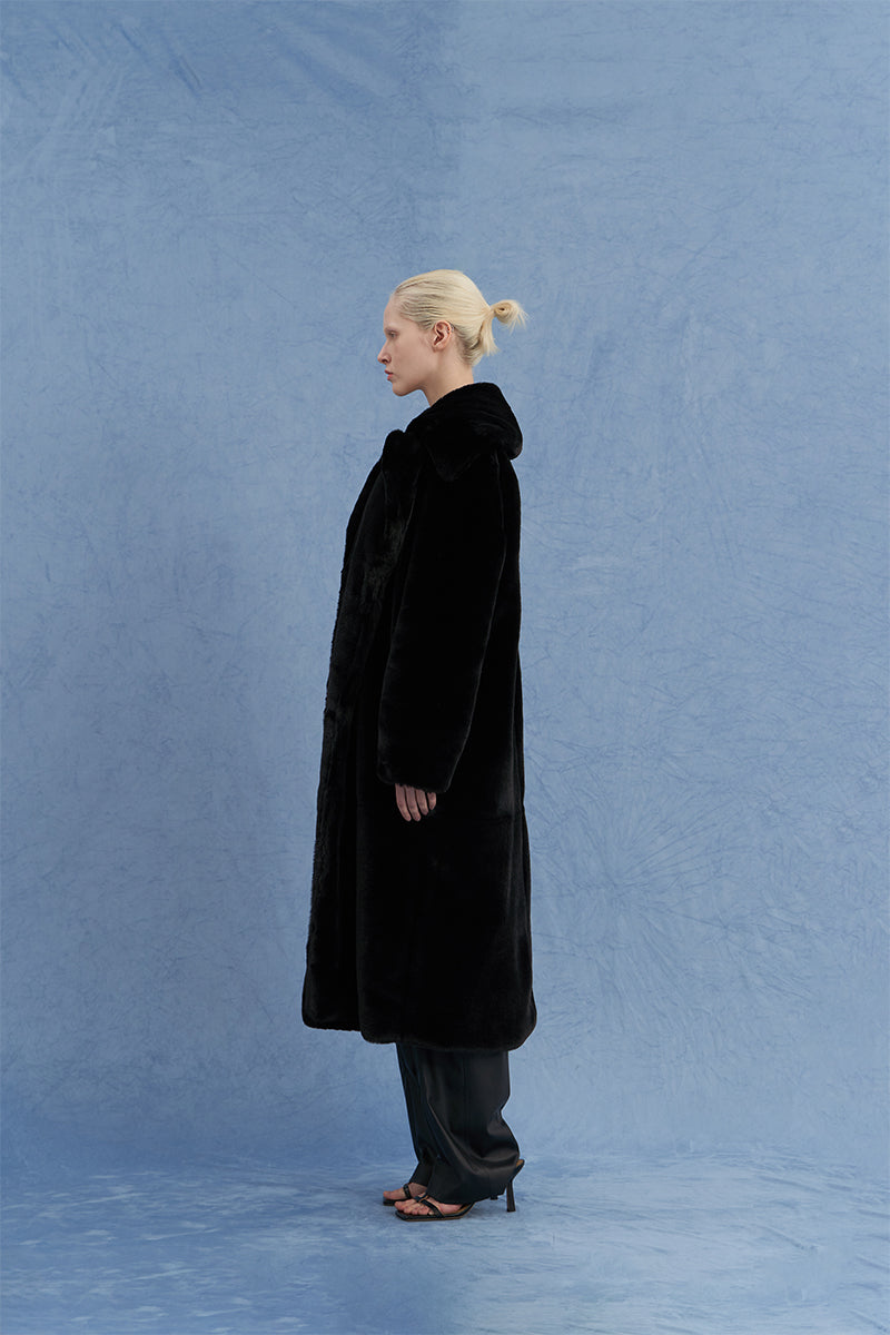 Black oversized shearling coat by JINSUN shown from the side, featuring a plush shearling collar and relaxed fit.