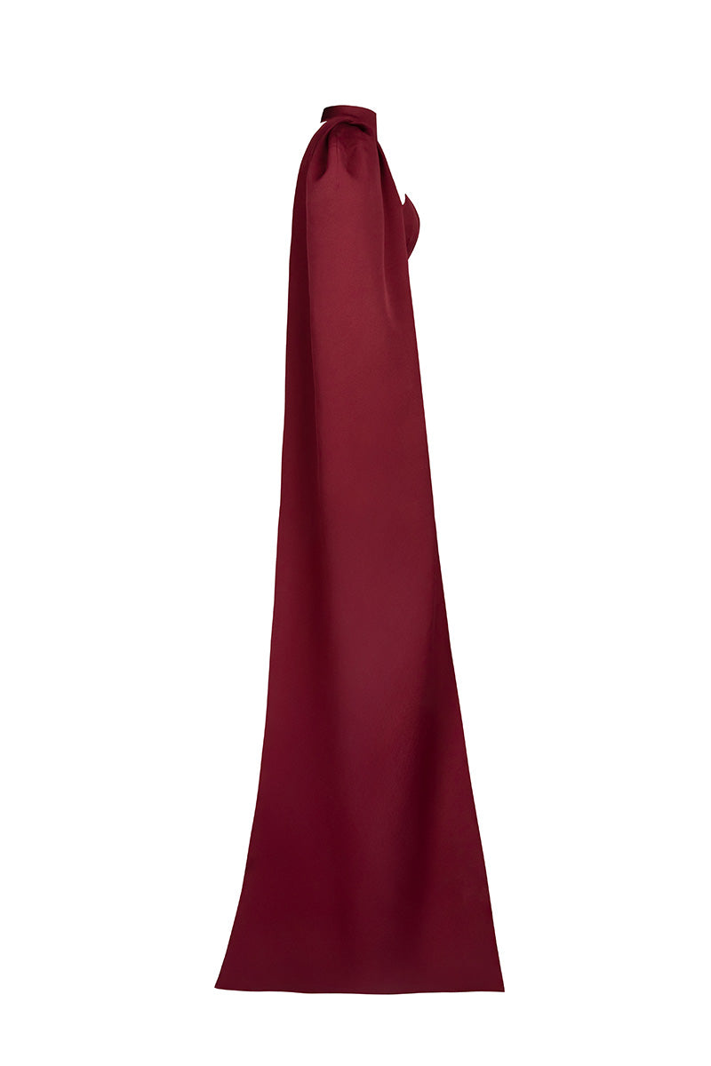 Joanna Andraos burgundy twist gown shown from the side, elegant evening gown with twisted fabric design and flowing silhouette.