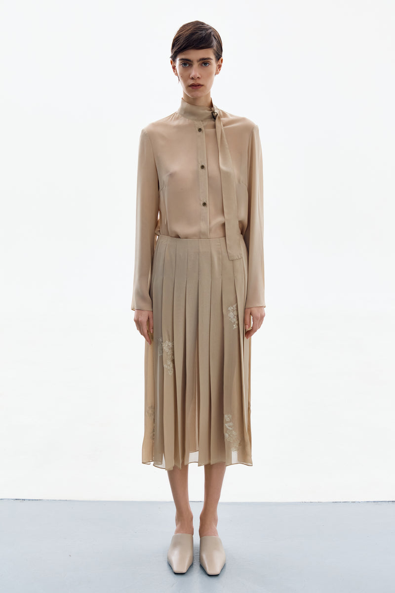 Golden nude pleated midi skirt by DELEGAN, shown from the front with a flowing, elegant design and soft fabric folds.